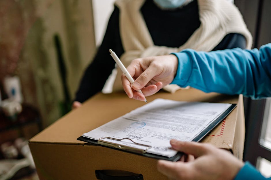 Close-up of a person signing a delivery document placed on a large cardboard box indoors.